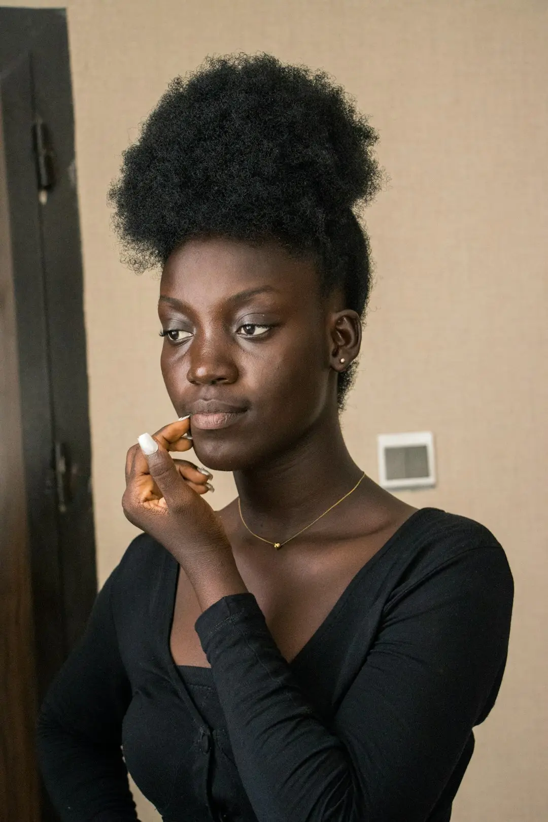 Mulher negra aplicando base líquida com esponja diante do espelho, luz natural suave